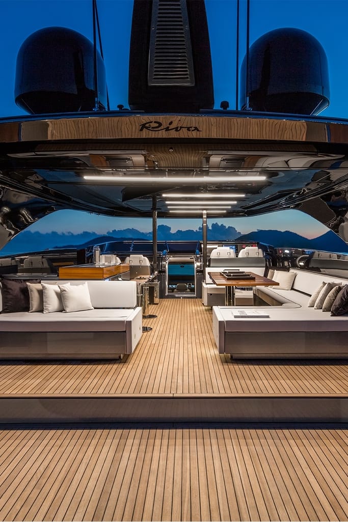 An opulent interior of the yacht, Riva 110' Dolcevita at dusk, showcasing elegant furnishing and soft orange lighting.